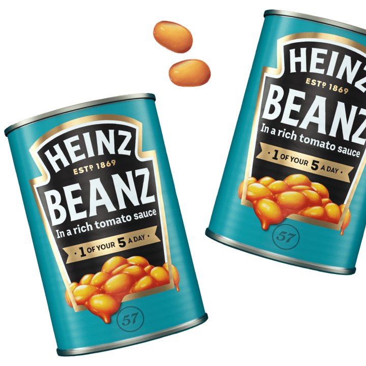Two cans of Heinz Beanz in rich tomato sauce, tilted against a black background, with a few loose beans.