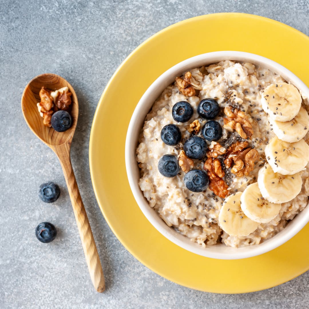 Havermout met banaan, bosbessen en walnoten in een kom op een geel bord.