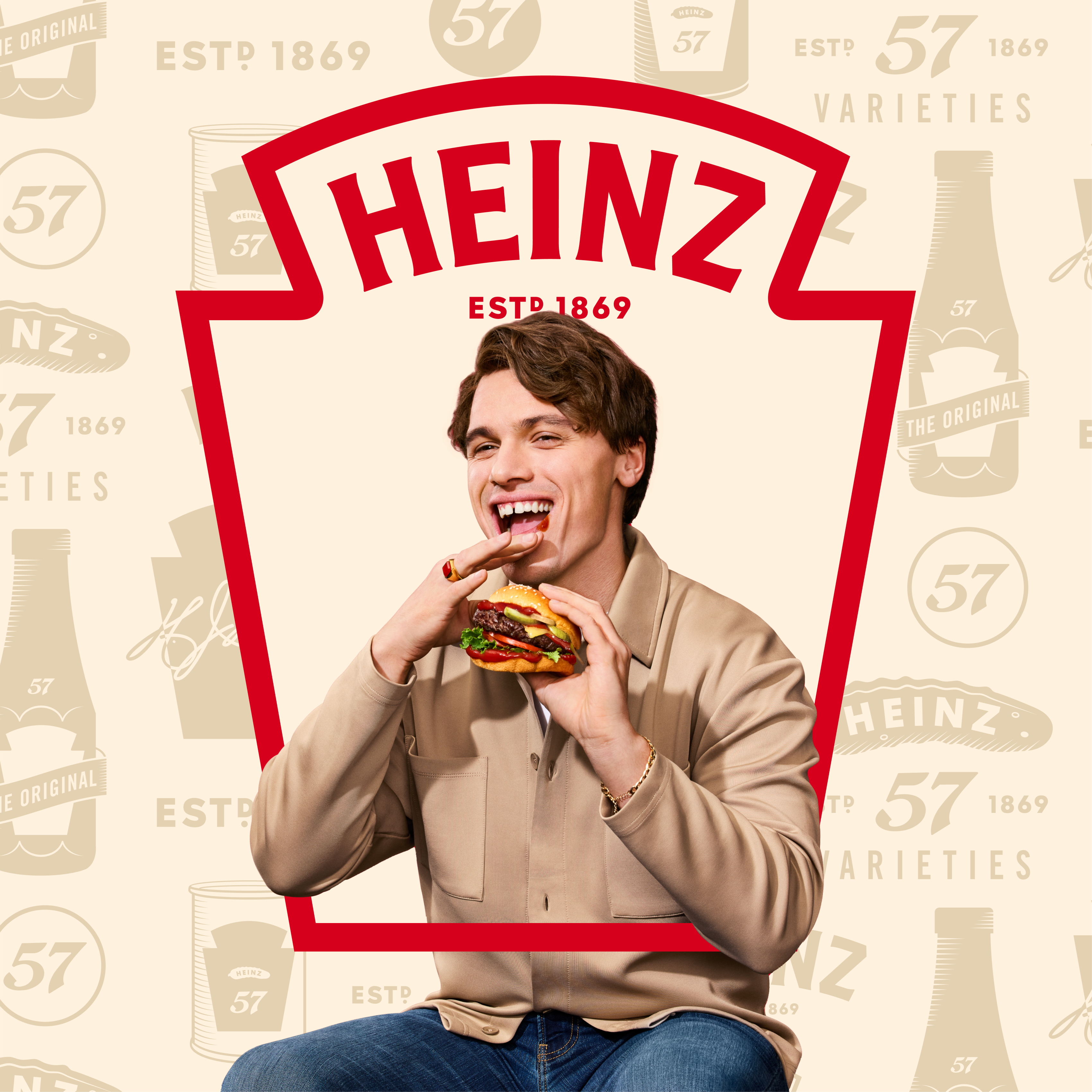 Against a cream backdrop patterned with vintage Heinz labels and the iconic '57 Varieties' logo, a young man sits holding a b