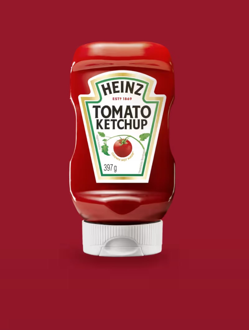 Uma garrafa de Heinz Tomato Ketchup com sua etiqueta verde e vermelha, sobre um fundo vermelho escuro.