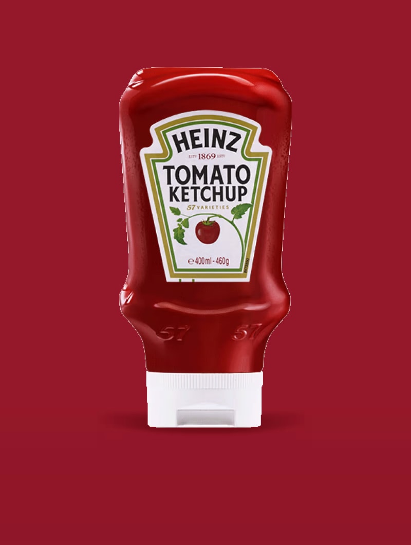 Mat, koyu kırmızı bir arka planın ortasında parlak, canlı kırmızı, baş aşağı duran bir Heinz Domates Ketçabı sıkma şişesi