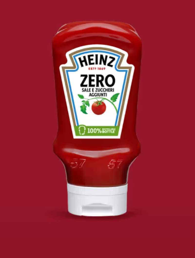 Una bottiglia squeeze di Heinz Zero Ketchup, rosso brillante e lucida, capovolta, è centrata su uno sfondo rosso scuro, opaco
