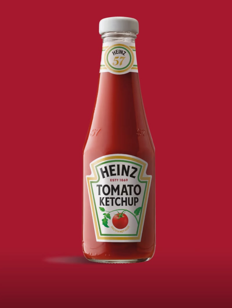 A classic glass bottle of Heinz Tomato Ketchup with its red contents and white label, set against a deep red background.
