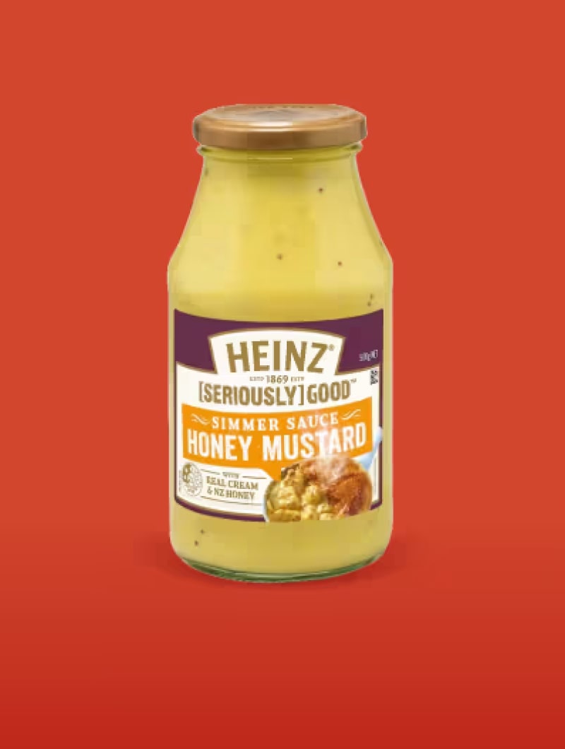 A glass bottle of Heinz [Seriously] Good Simmer Sauce Honey Mustard, against an orange-red background.