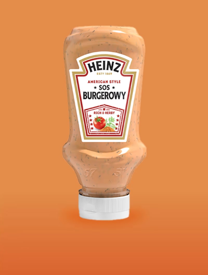 Odwrócona butelka sosu Burgerowego American Style Heinz wyśrodkowana na jednolitym, ciepłym pomarańczowym tle.