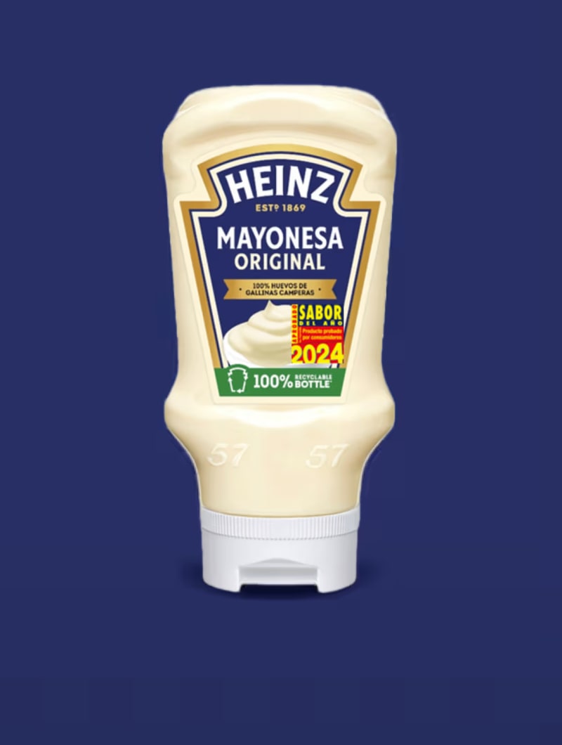 Una botella de Mayonesa Original Heinz con tapón blanco, sobre un fondo azul oscuro liso. La etiqueta muestra "HEINZ ESTD 186