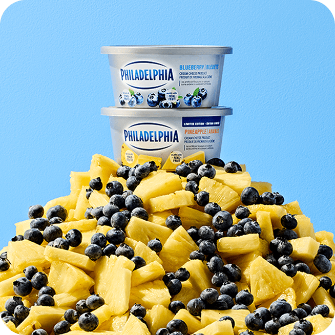 Deux contenants de fromage à la crème Philadelphia, saveurs Bleuet et Ananas, posés sur un monticule de bleuets frais et de m
