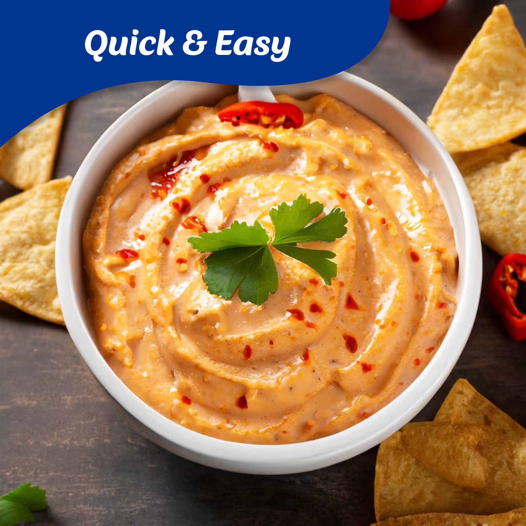 Creamy orange dip with red chili flakes and a parsley sprig in a white bowl, surrounded by tortilla chips.