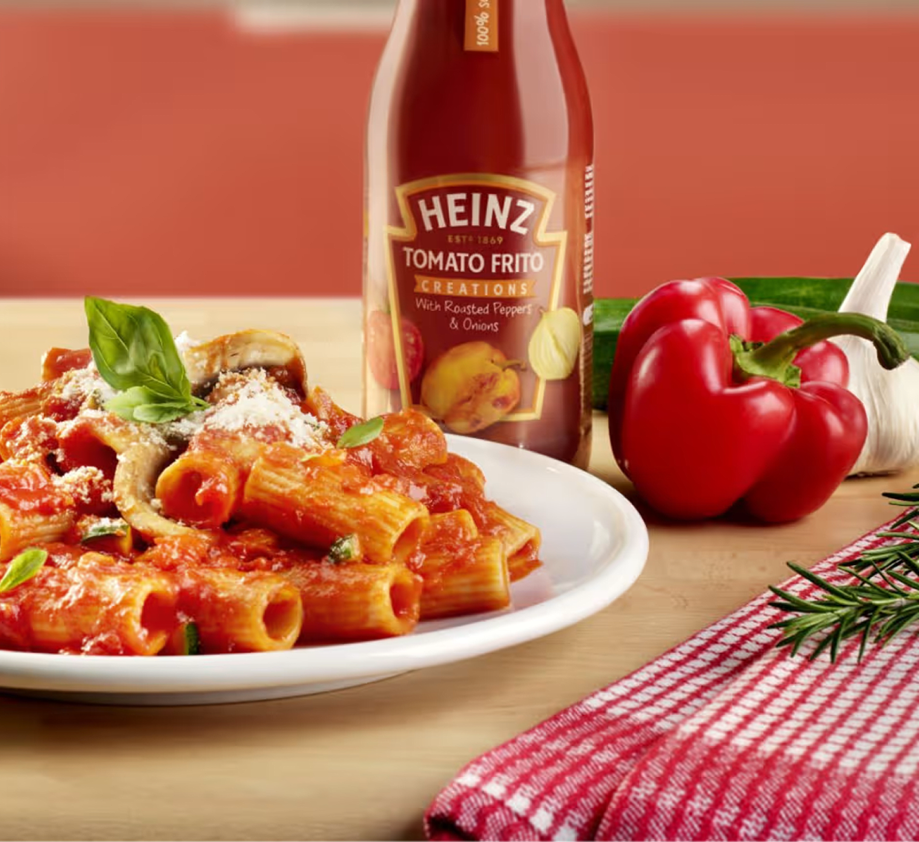 Een bord pasta met Heinz Tomato Frito Creaties, gegarneerd met basilicum en Parmezaanse kaas, met een fles Heinz Tomato Frito