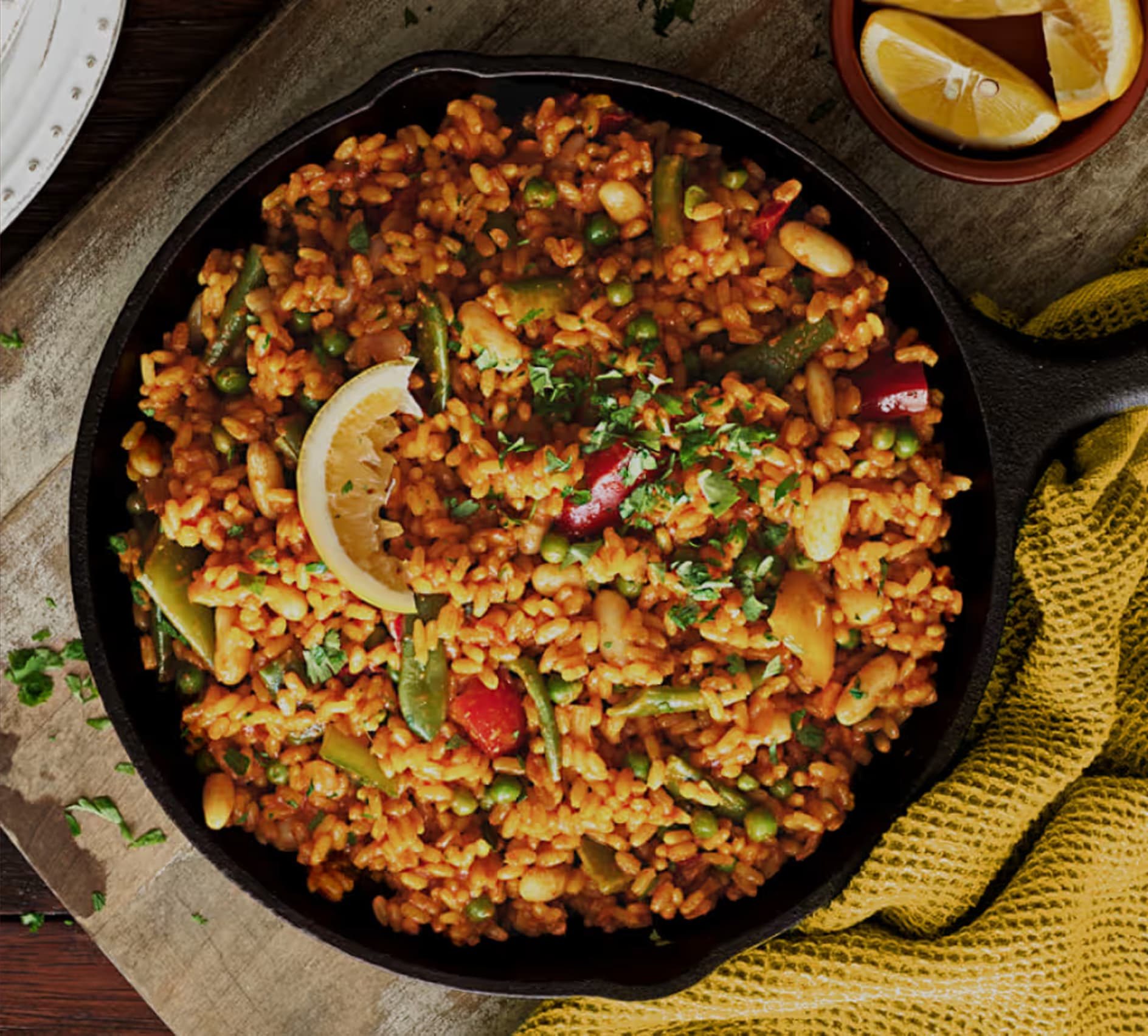 Imagen tipo banner presentando una paellera de hierro fundido negra llena de un plato de arroz estilo paella de verduras