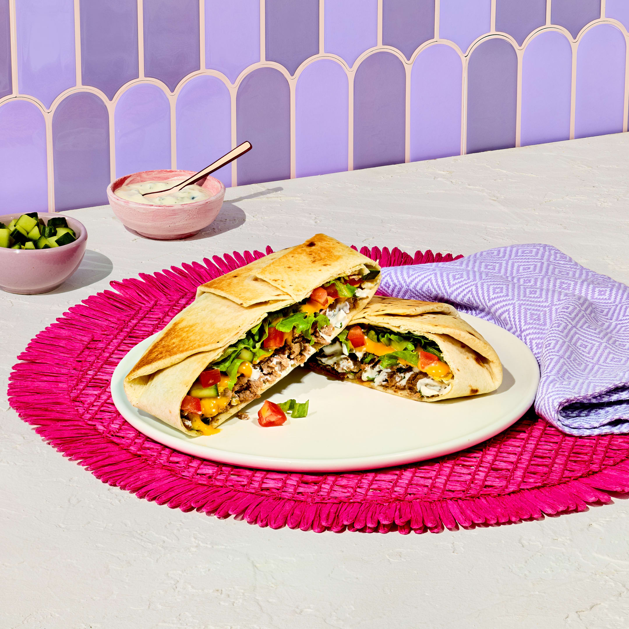 Greek Style Gyro Crunchwrap cut in half on a white plate showing meat, lettuce, tomatoes, and tzatziki filling