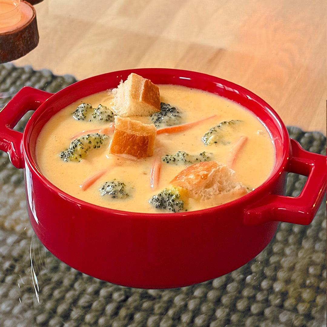 A bowl filled with creamy broccoli cheese soup. The soup contains broccoli florets, carrot strips, and bread croutons. 