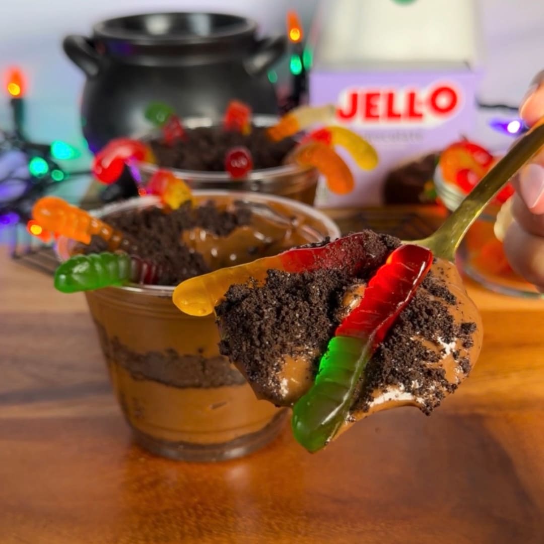 Spoonful of JELL-O chocolate pudding dirt cup topped with cookie crumbs and a gummy worm