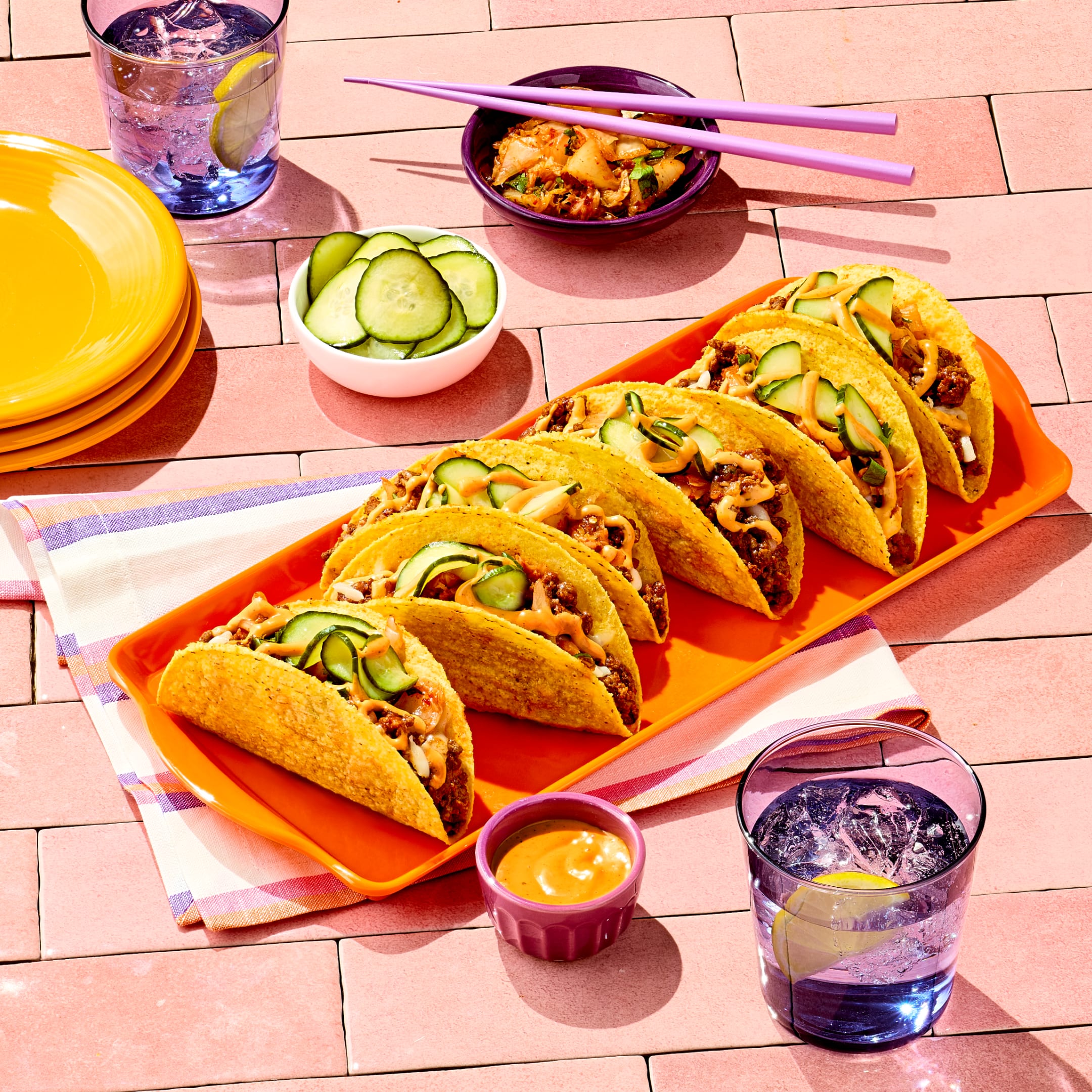 KBBQ Tacos on an orange platter topped with sliced cucumbers and a drizzle of sauce