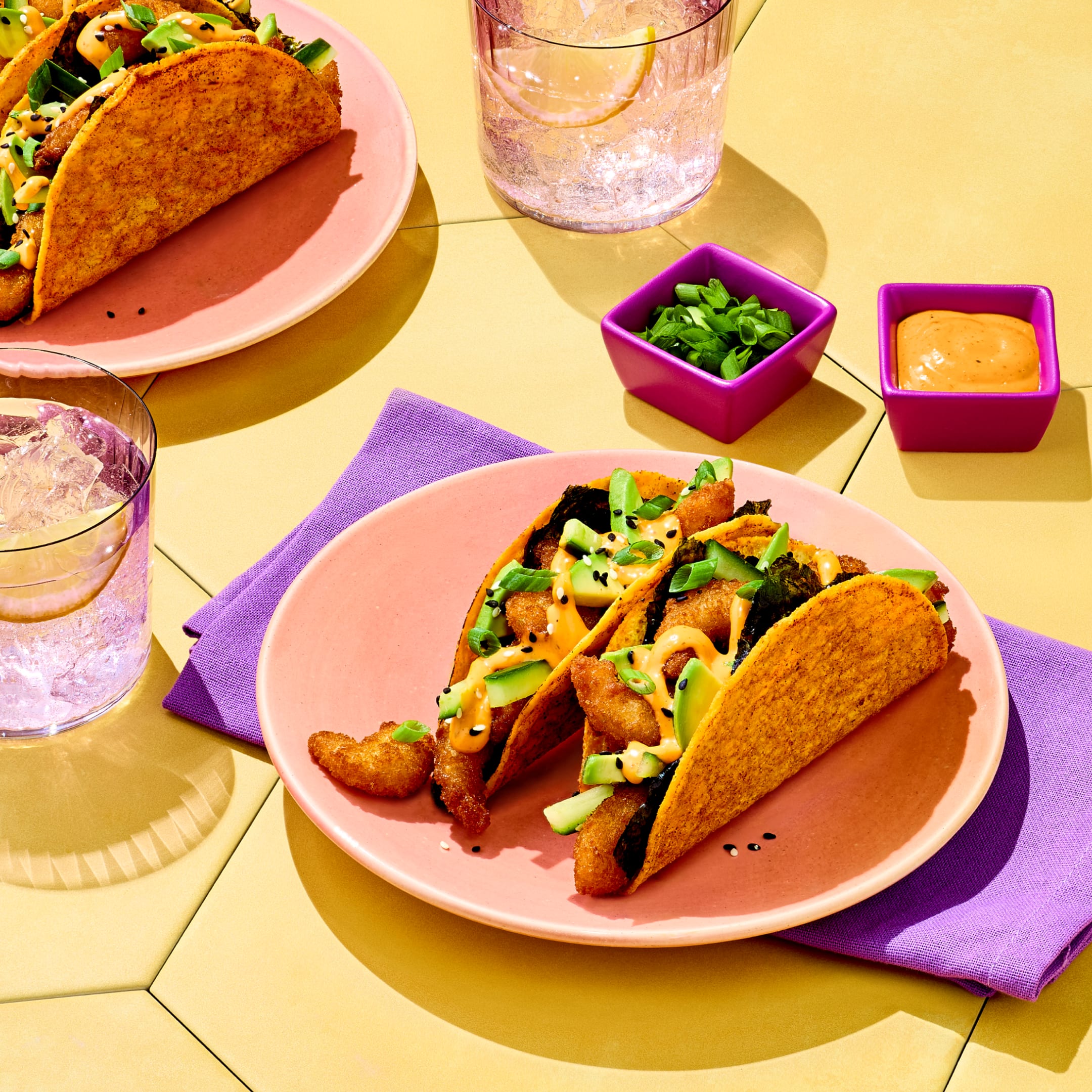 Shrimp Volcano Roll Tacos on a pink plate topped with sliced avocado and spicy sauce