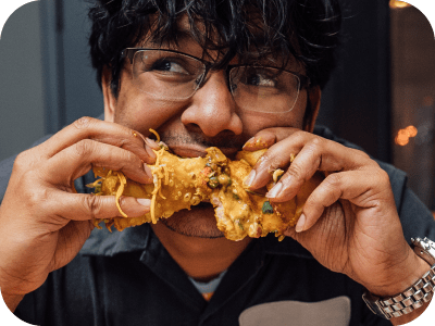 Man with glasses eating a fried food roll.