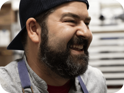 A bearded man wearing a cap smiles.
