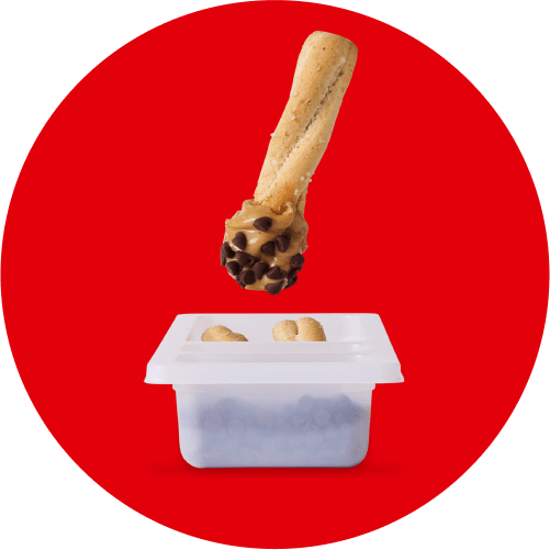 A breadstick dipped in peanut butter and chocolate chips is poised above a small container of additional breadsticks, set against a bold red circular background. This image highlights a sweet and savory snack option within a Lunchables meal.