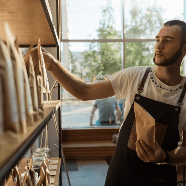 Un homme en tablier range des sacs de café sur une étagère.