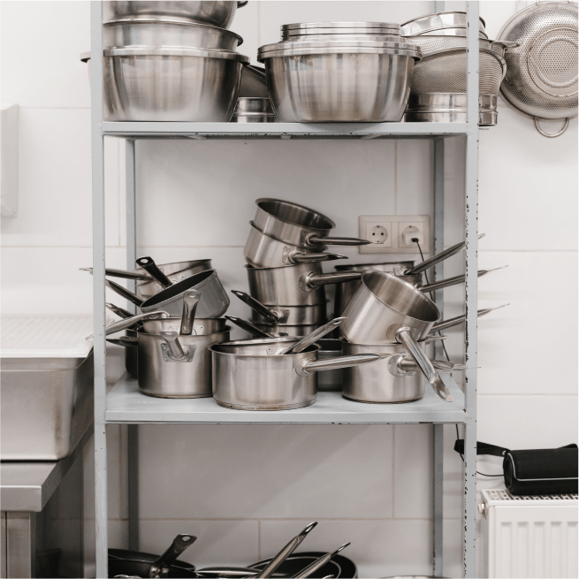 Metal shelves filled with stainless steel pots and pans in a kitchen.