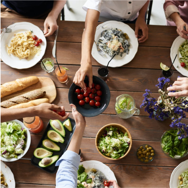 Overhead shot of a wooden table laden with plates of food, salads, and drinks.