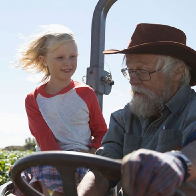 Un granjero anciano conduciendo un tractor con su nieta.
