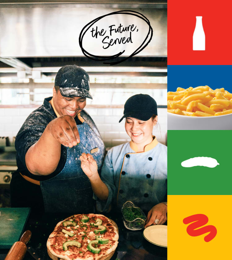 Two chefs prepare a pizza in a restaurant kitchen.