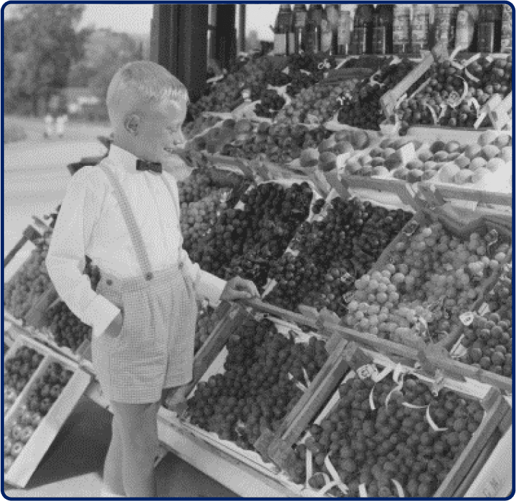 Een historische foto van een kleine jongen op een fruitmarkt.