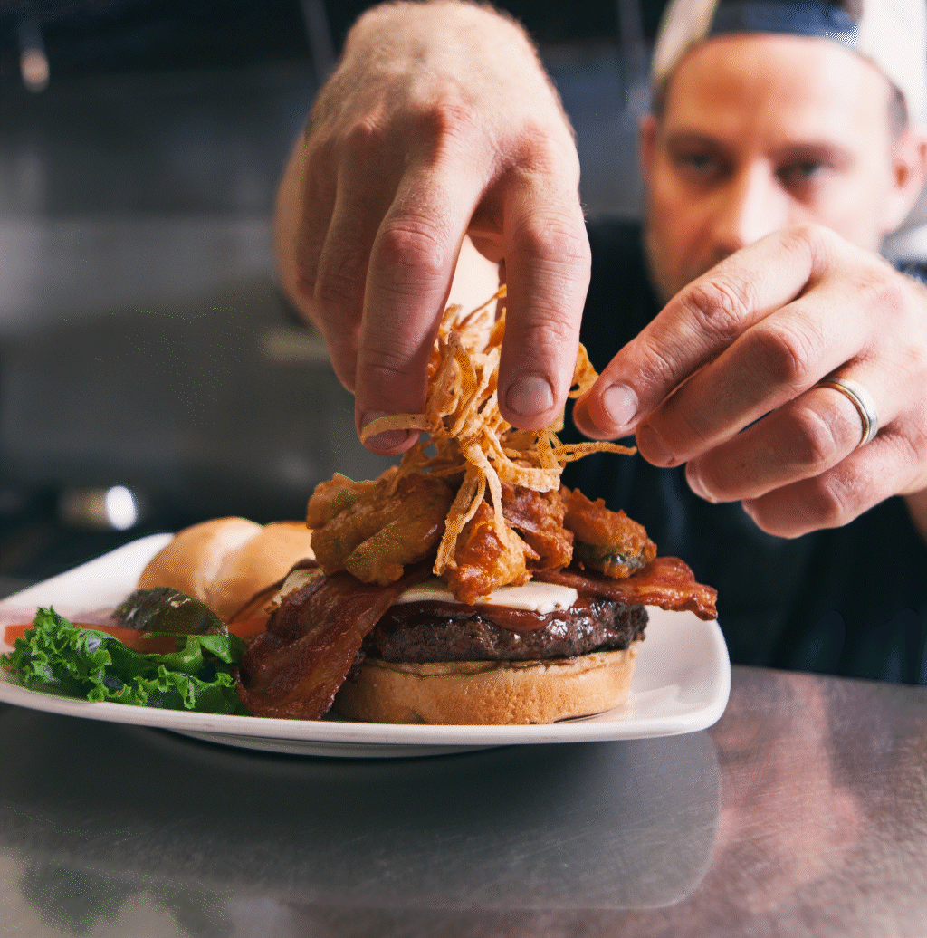 Un chef masculin garnit un burger avec des oignons frits.