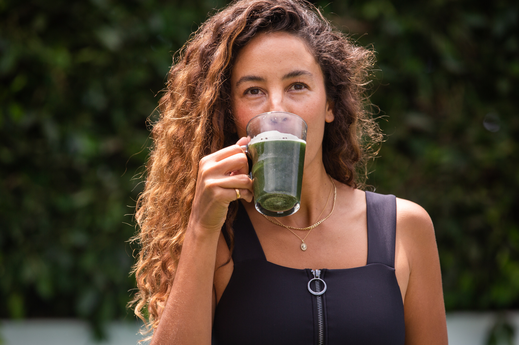 A woman drinking a glass of Kroma Supergreens Elixir.