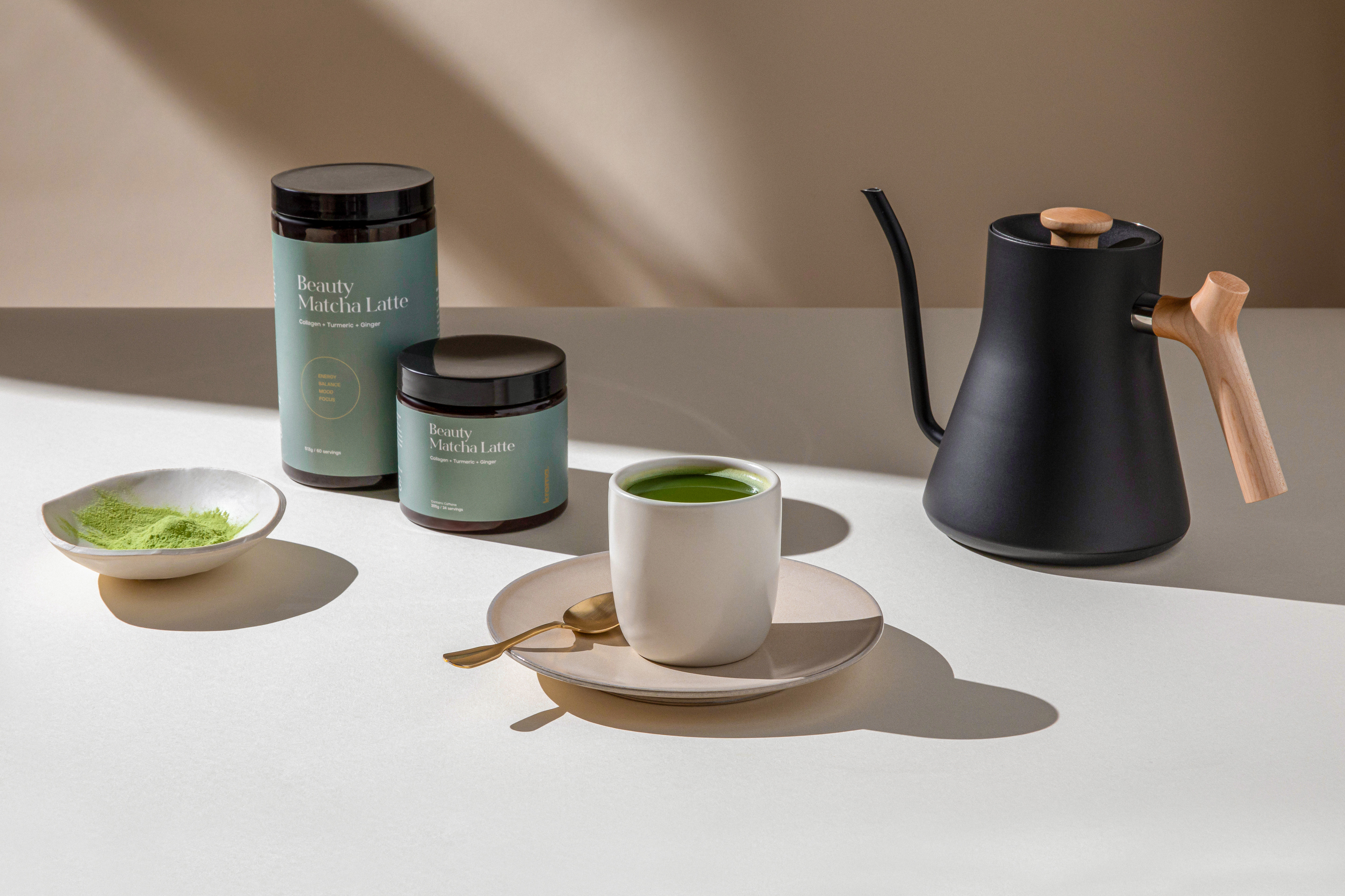 A prepared mug of Kroma Beauty Matcha Latte next to two jars of Beauty Matcha Latte.