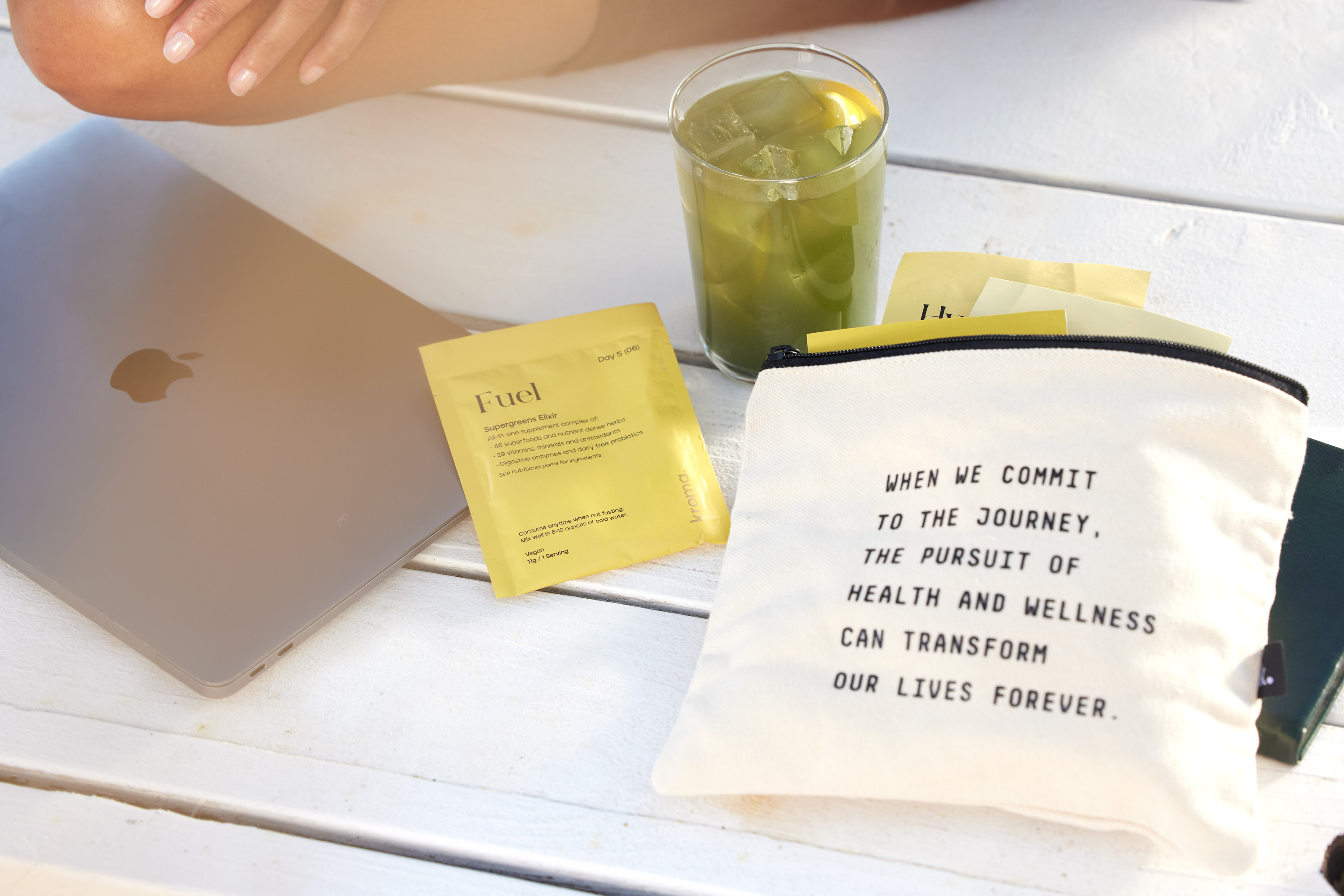 A glass of Kroma Supergreens Elixir with sachet, next to a Kroma inspirational Zipper Bag.