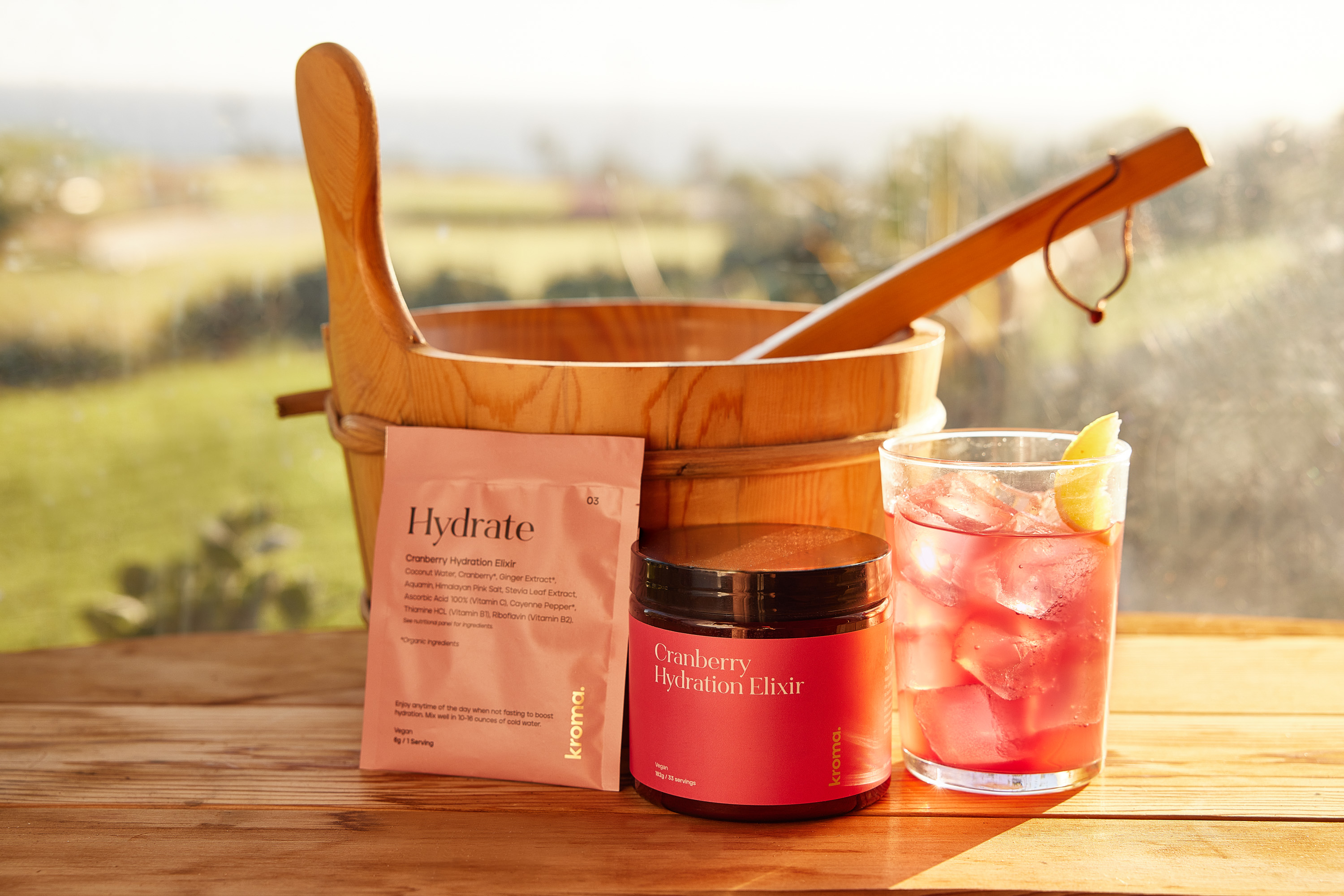 A glass, jar, and sachet of Kroma Cranberry Hydration Elixir.