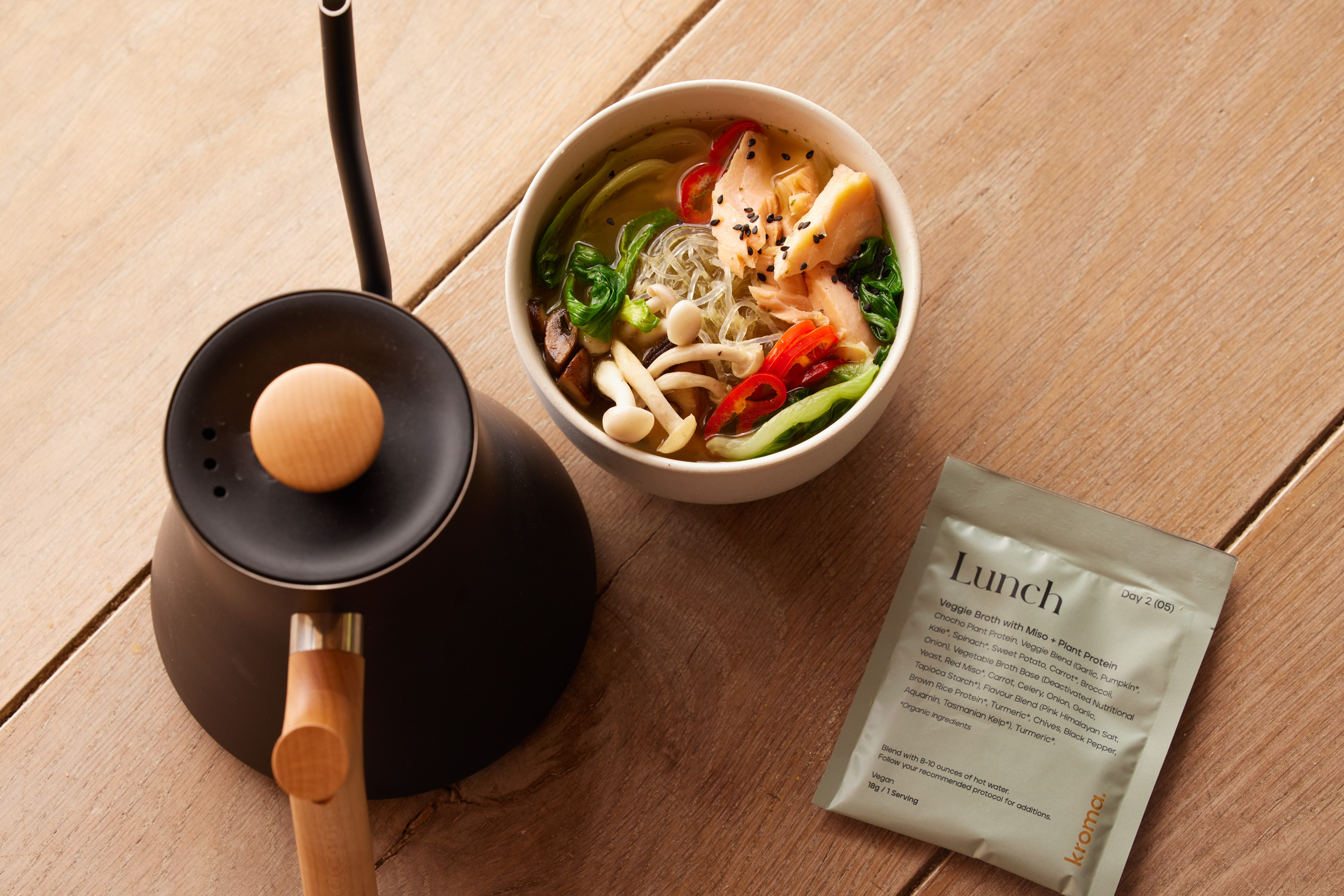 A bowl of healthy veggie soup next to a Kroma Veggie Broth with Plant Protein sachet.