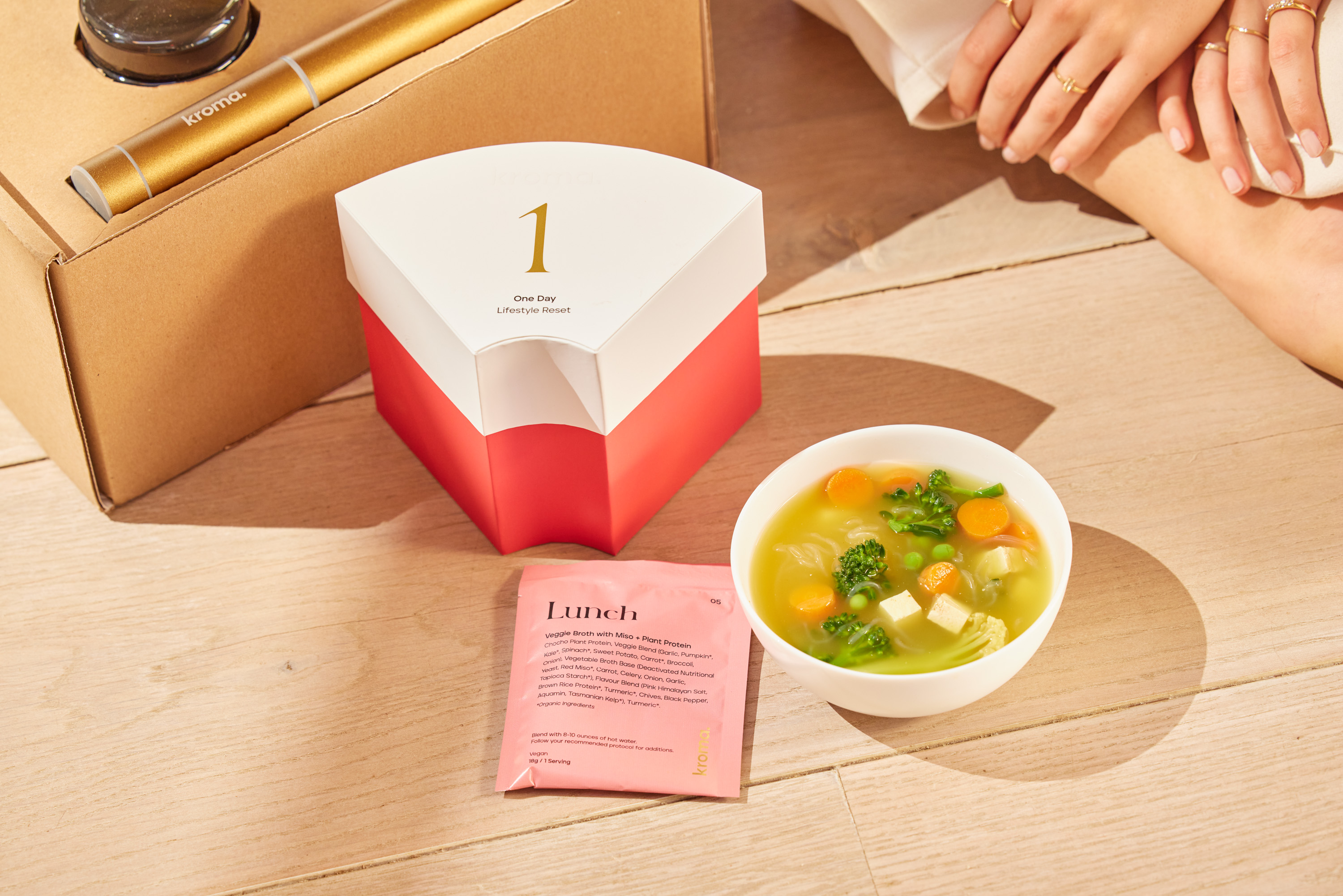 A bowl of healthy veggie soup next to a sachet of Kroma Veggie Broth with Plant Protein and 1 Day Reset pack.