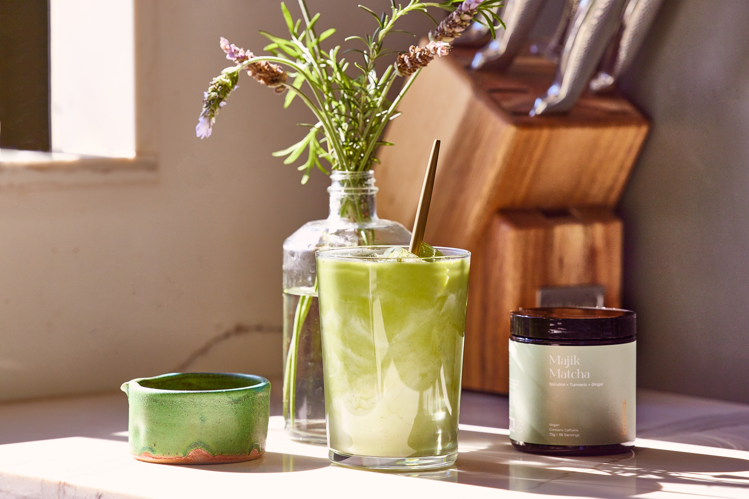 A glass of iced Kroma Majik Matcha latte beside a jar of Majik Matcha.