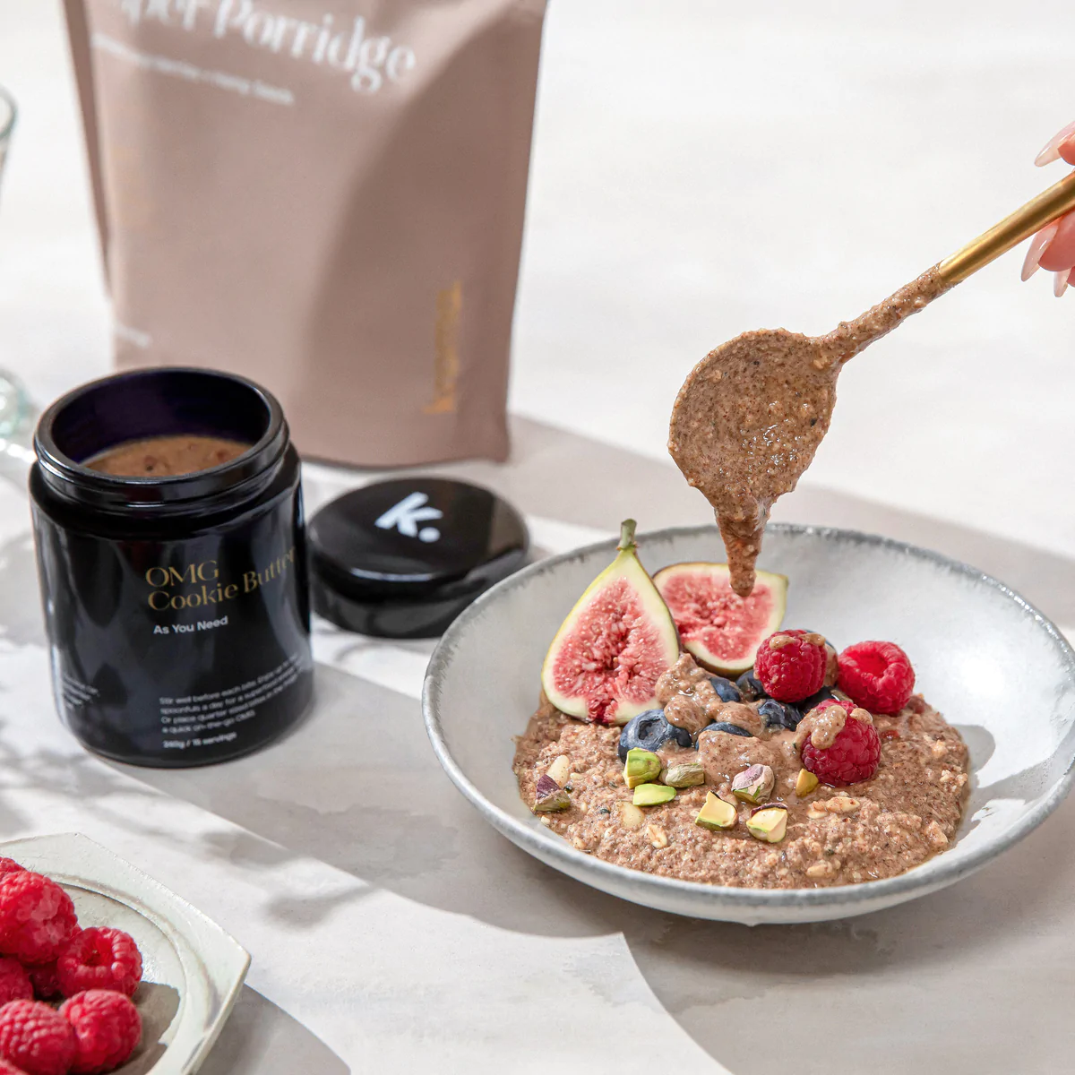 A bowl of prepared Kroma Super Porridge with fruit, next to an open jar of Kroma OMG Cookie Butter.