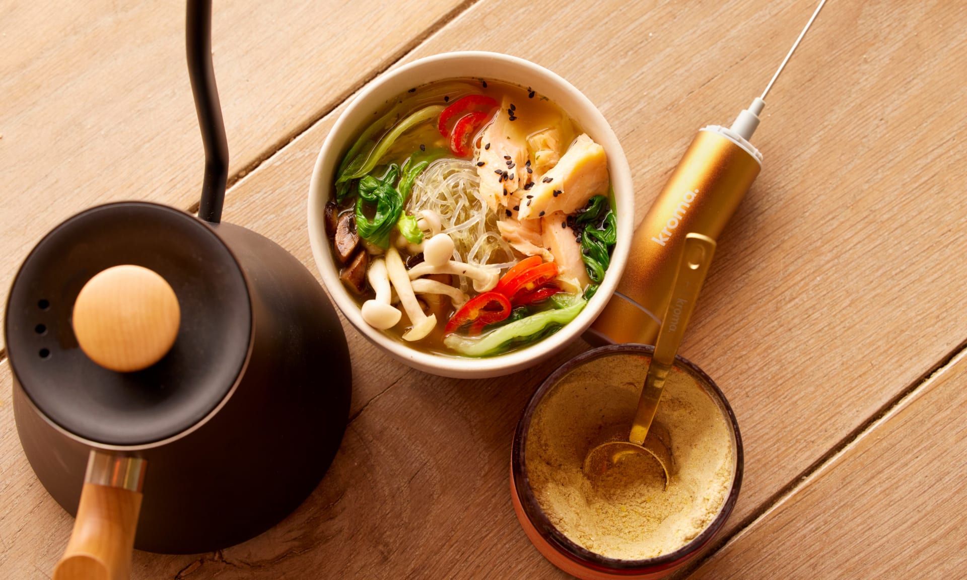 A bowl of healthy chicken soup next to a jar of Kroma 24K Chicken Bone Broth.