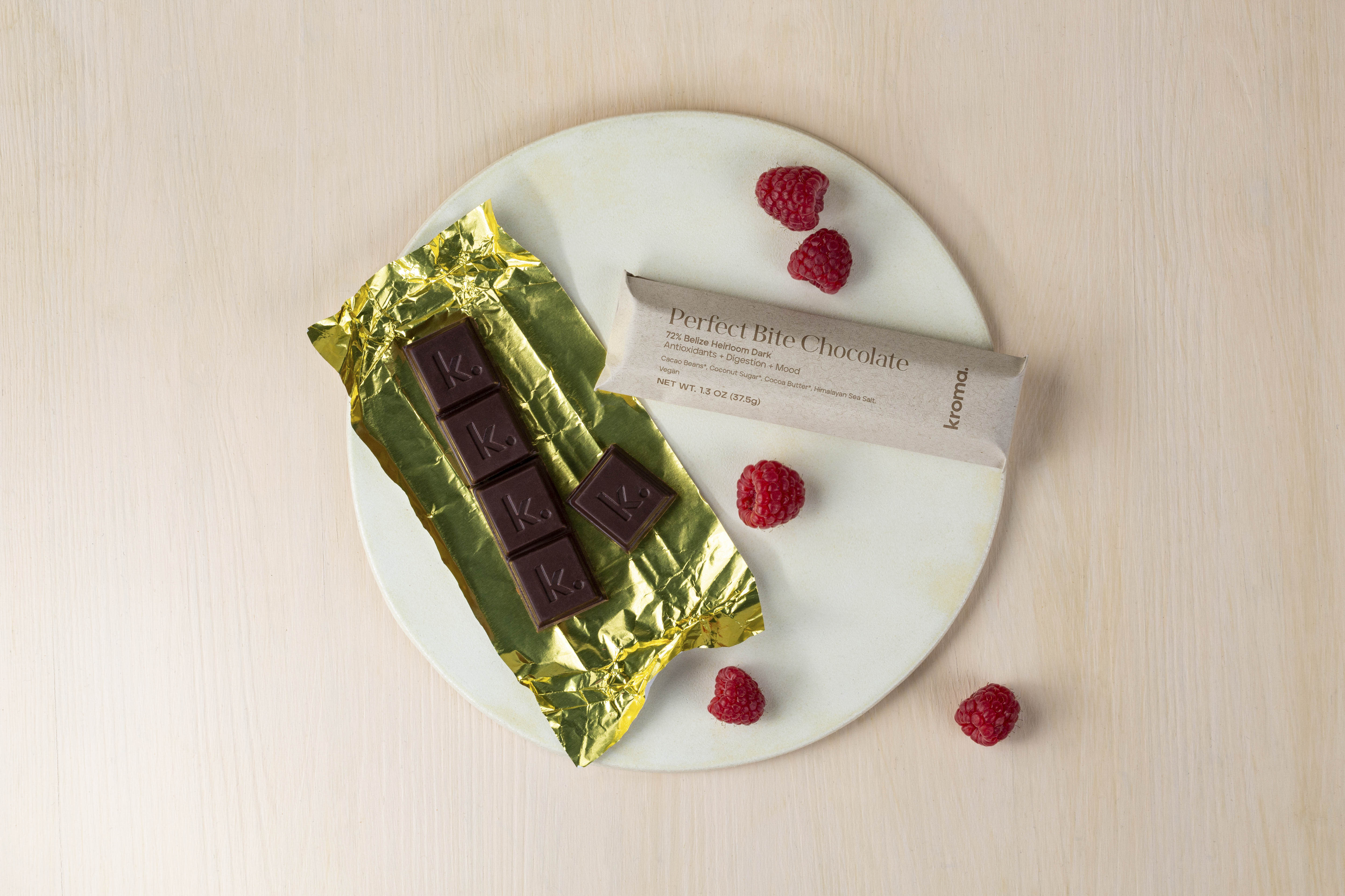 An unwrapped and wrapped bar of Kroma Perfect Bite Chocolate sitting on a plate.