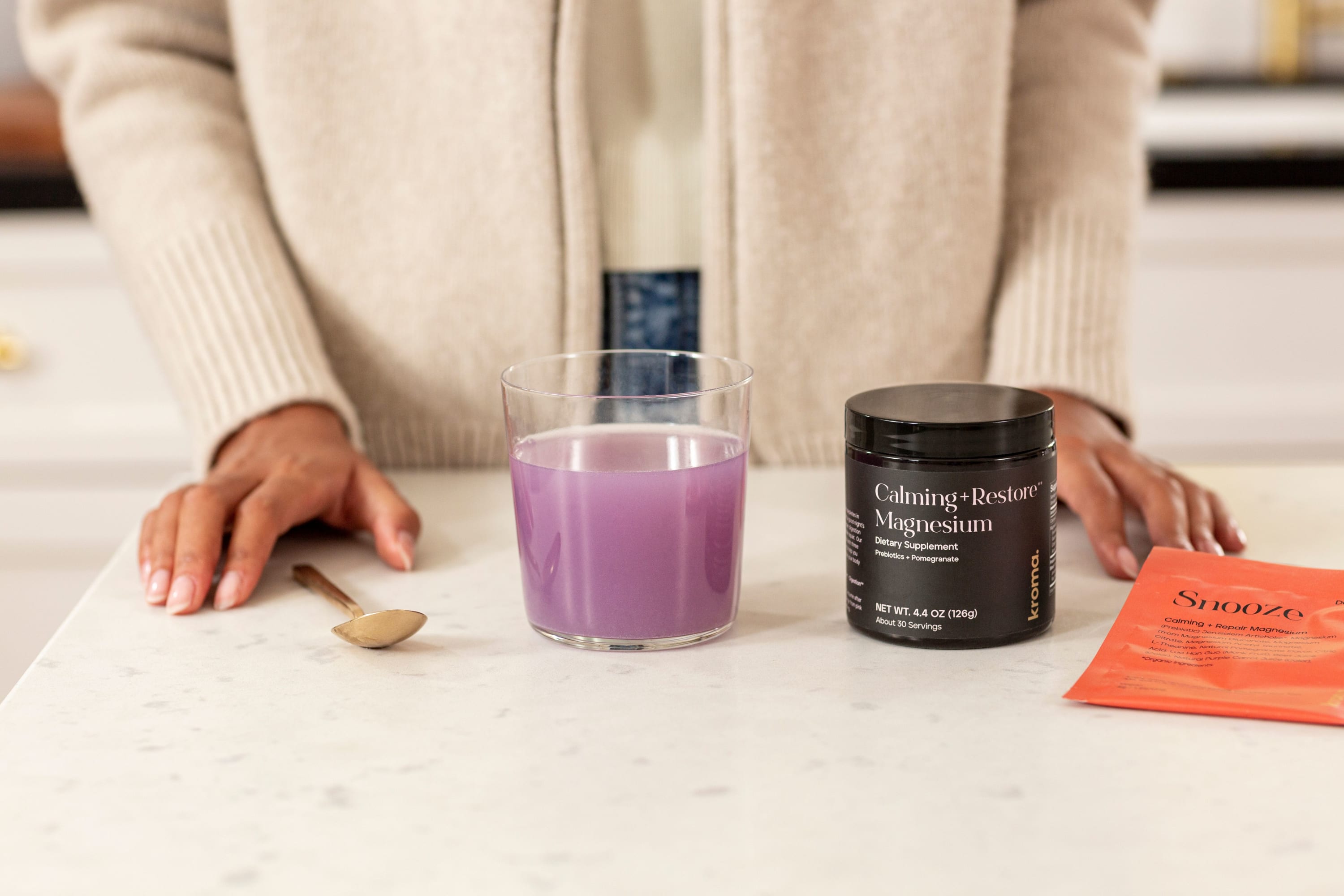 A woman standing behind a glass of prepared Kroma Calming + Restore Magnesium next to its jar.