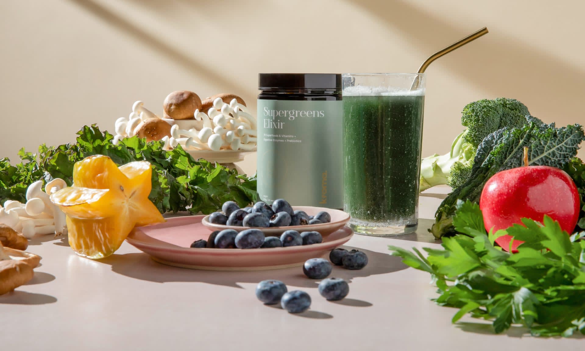 A glass of Kroma Supergreens Elixir surrounded by fresh fruits and veggies.