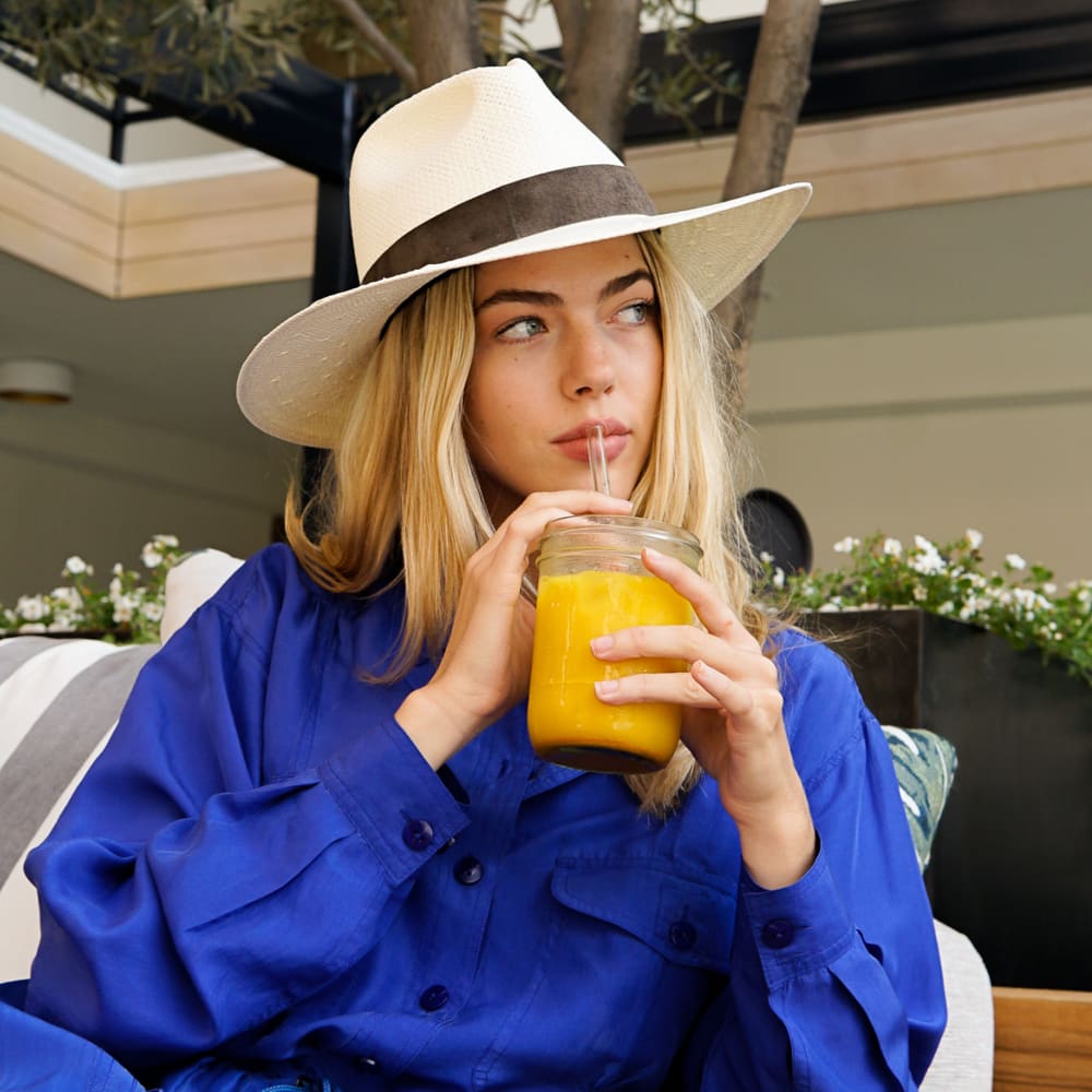 A woman drinking a glass of Kroma Ultimate Vitality Latte with a straw.