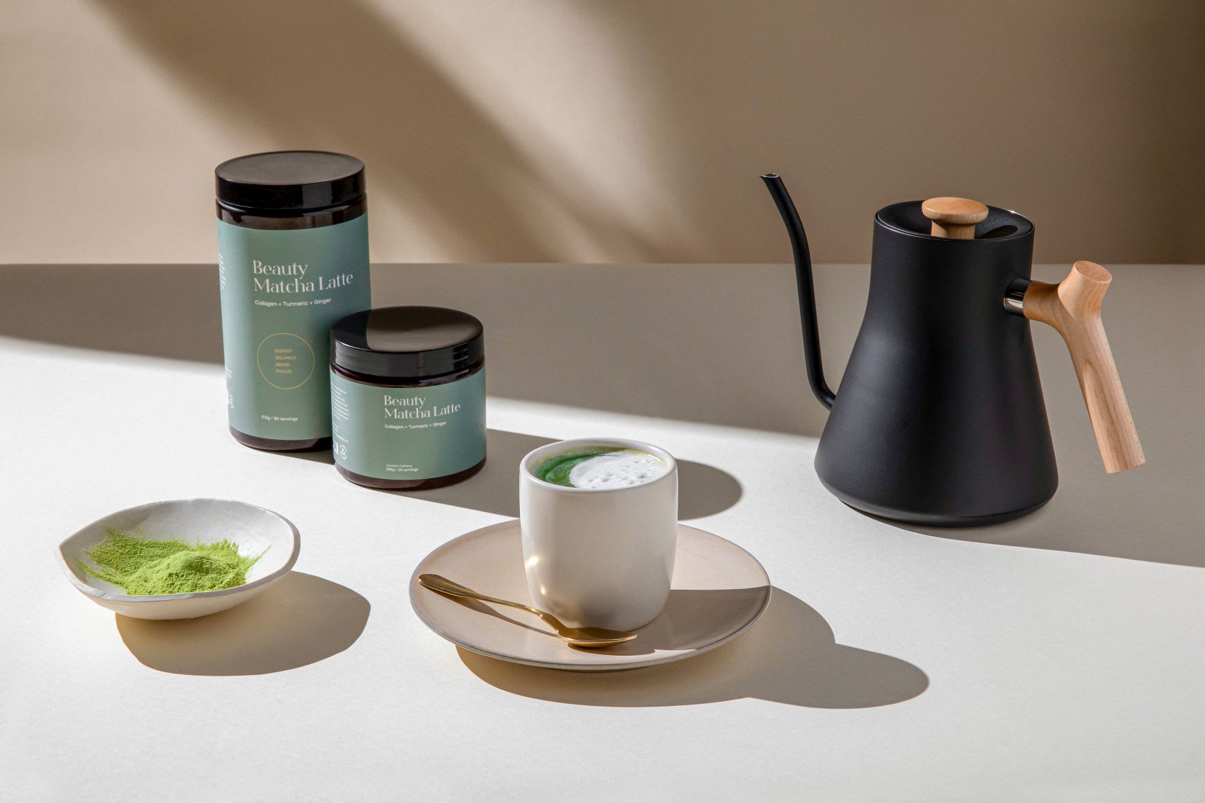 A prepared mug of Kroma Beauty Matcha Latte next to two jars of Beauty Matcha Latte.