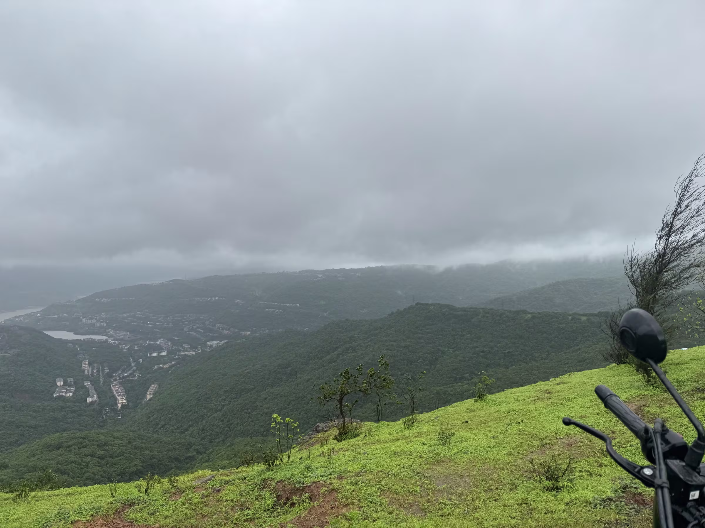 Motorcycle cockpit view looking out over the expansive green valley and hills at Lavasa ghat viewpoint