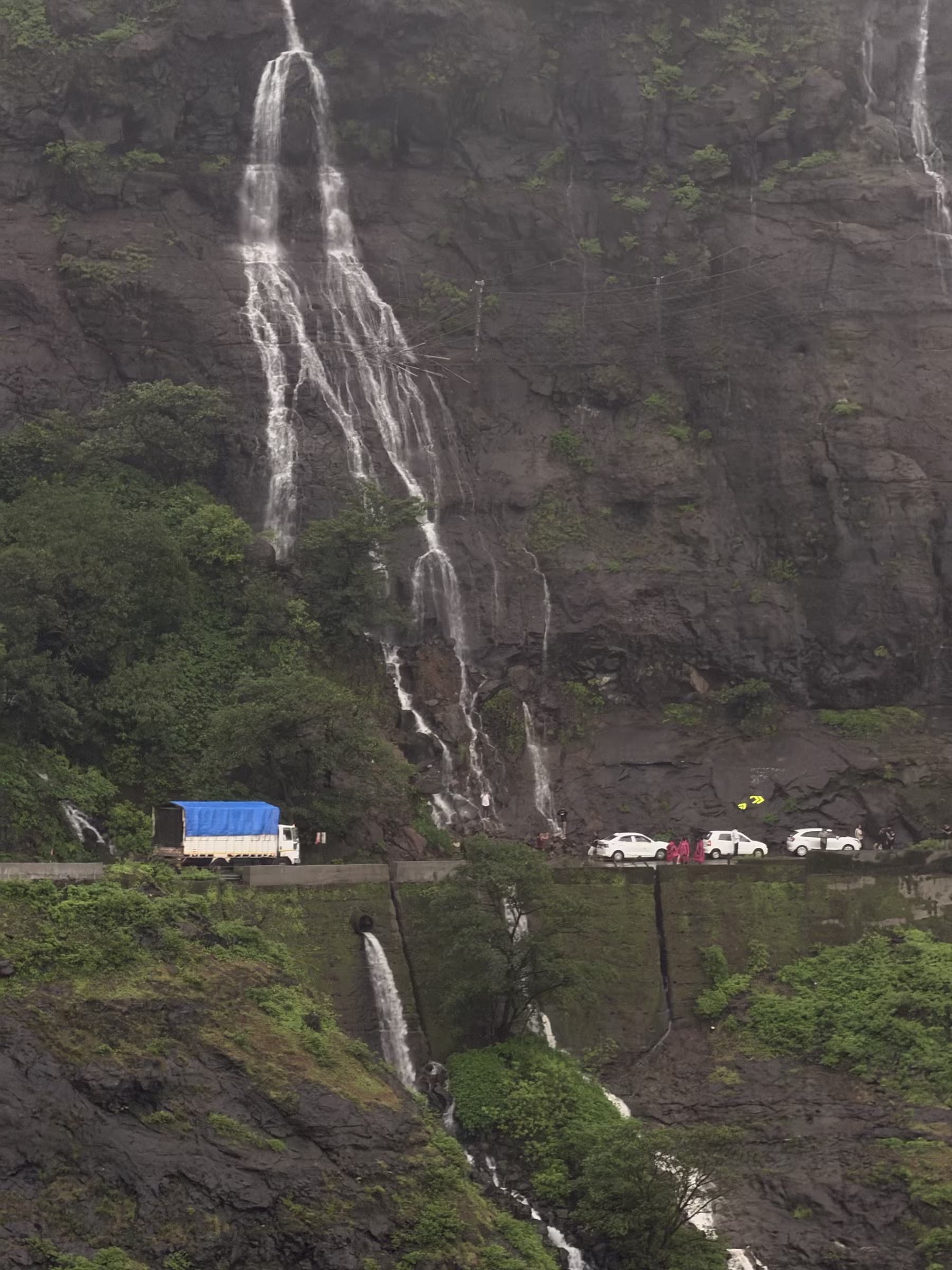 Vehicles passing under roadside rock waterfalls carved into the mountain cliffs of Malshej Ghat