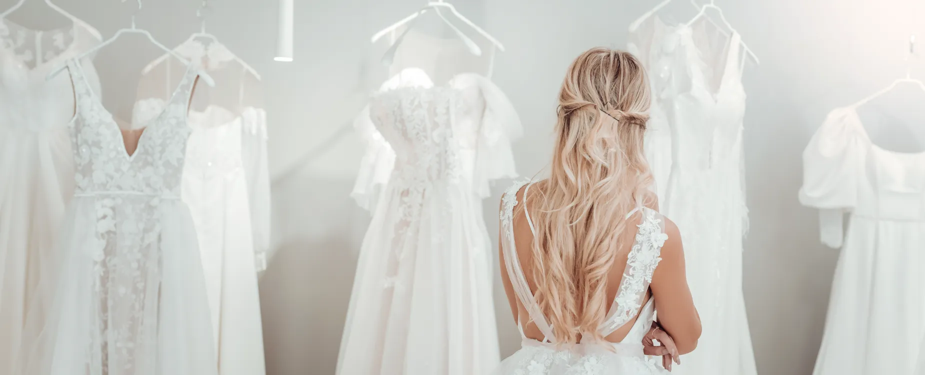 Image of a woman wearing a wedding dress and browsing other wedding dresses that are hanging on hangers