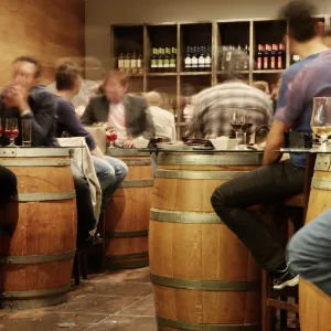 image inside a wine tasting room with people sat at barrell style tables
