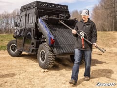 Man carrying the removed winch crossbar away from a blue Polaris Ranger Crew with its bed tilted.