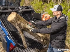 Man holding a chainsaw guides a log into the tilted bed of a blue Polaris Ranger as the winch pulls it in.