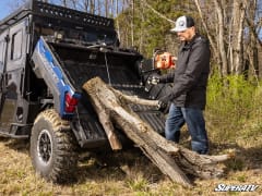 Blue Polaris Ranger Crew with its dump bed tilted while the winch pulls a log up into it.